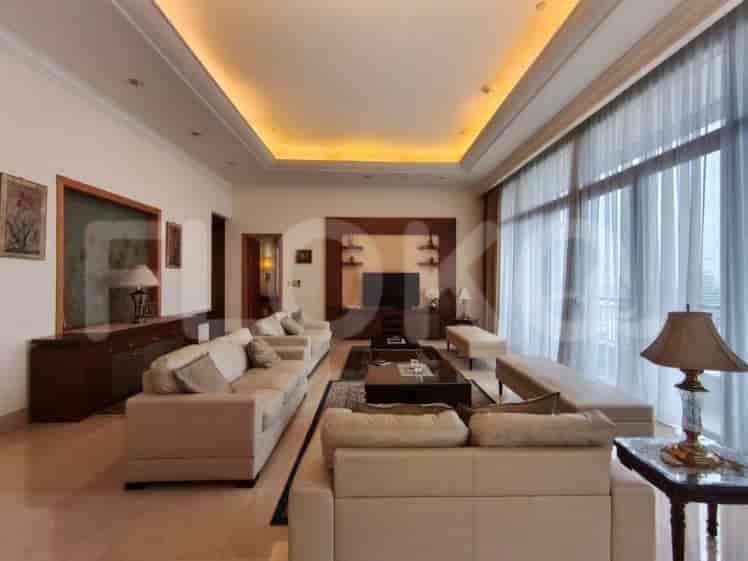 A spacious living room with multiple sofas, a large TV, a coffee table, and floor-to-ceiling windows with sheer curtains.