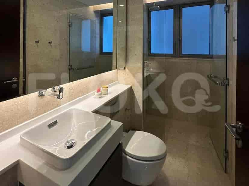Modern bathroom with a sink, toilet, and a glass shower enclosure. Neutral stone-like tiles cover the floor and walls.
