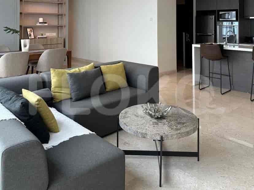 A modern living room featuring a grey sofa, round marble coffee table, and an open view into the kitchen.
