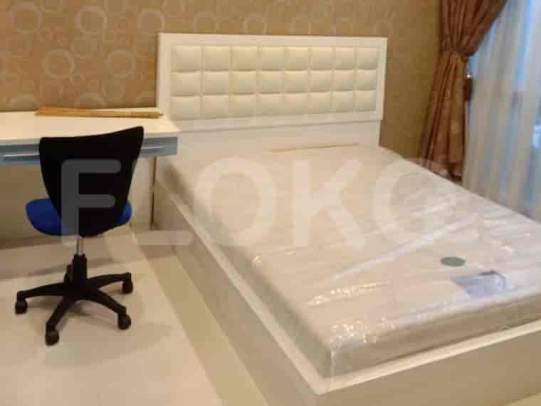 A white bed with a cushioned headboard, a white desk, and a black office chair.
