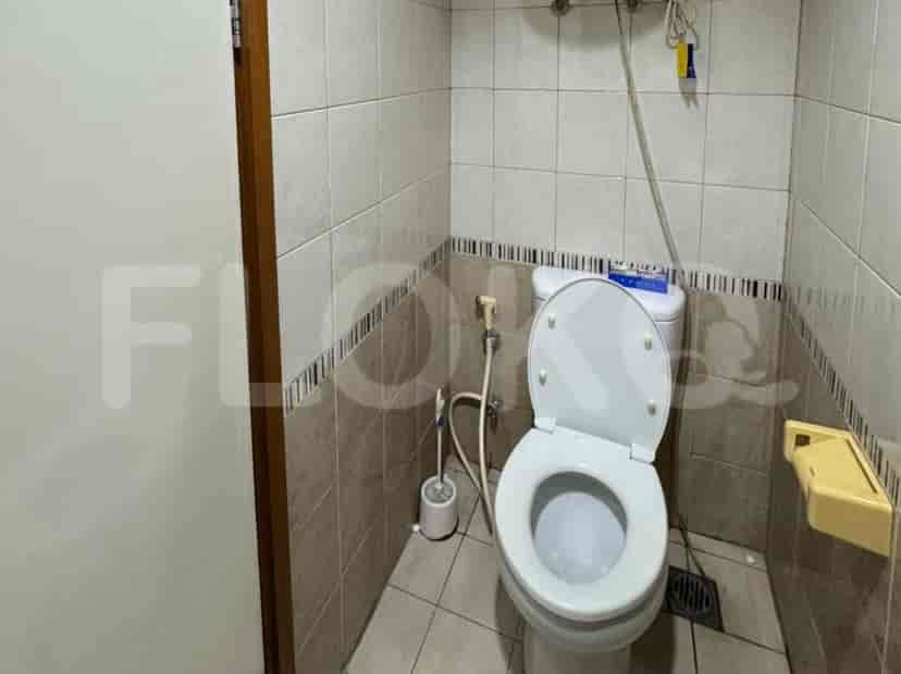 A small bathroom with a toilet, tiled walls, and a wall-mounted toilet brush holder.