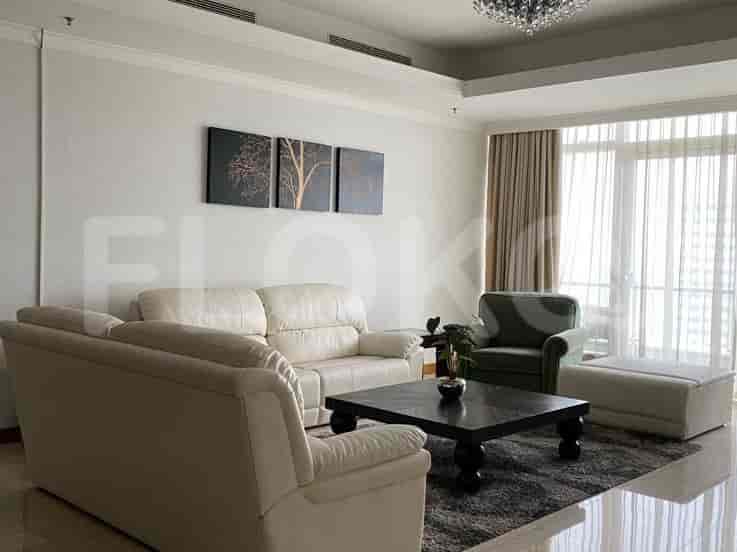 Ruang tamu yang terang dengan sofa besar berbentuk L, meja kopi, dan tirai tipis yang menutupi jendela besar.