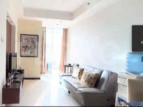 Ruang tamu modern dengan sofa abu-abu, TV pintar, dan pemandangan melalui gorden tipis.