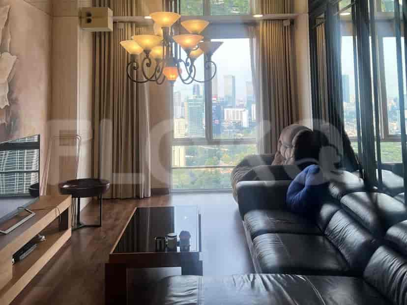 Ruang tamu dengan sofa kulit cokelat tua, meja kopi, dan pemandangan kota melalui jendela besar.