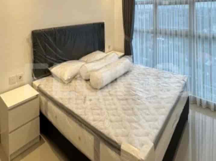 A bedroom furnished with a queen-sized bed, covered in plastic wrap, with two bedside tables and a large window with sheer curtains.
