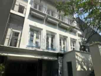 A multi-story building with a white facade, balconies, and a covered entrance.