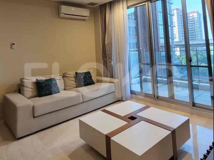 A living room with a light beige sofa, a large square coffee table, and a sliding glass door leading to a balcony.