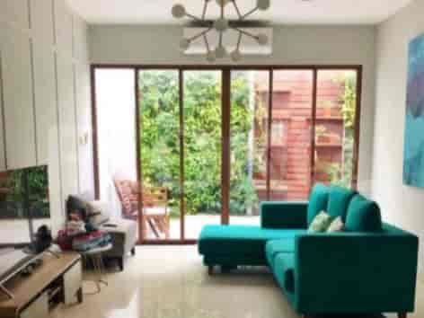 A modern living room with a teal sectional sofa, large windows offering a garden view, and a chandelier.