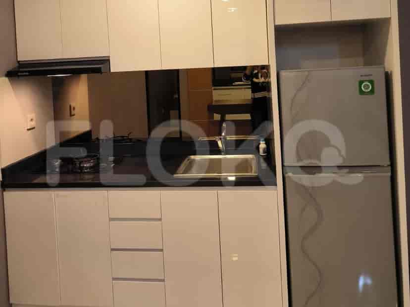 Area dapur ringkas dengan kabinet putih, meja kerja hitam, dan kulkas.