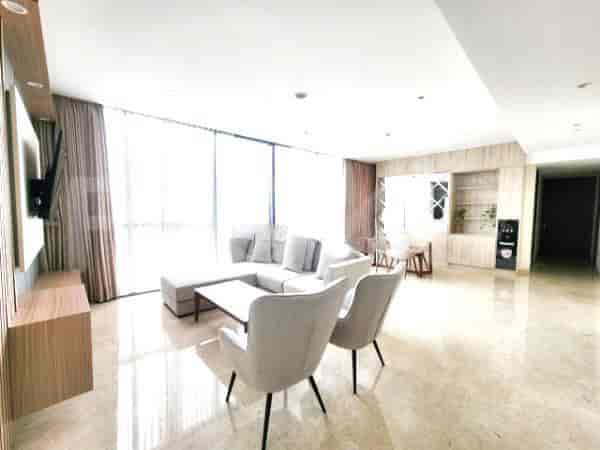 A spacious living room with an L-shaped grey sofa, wall-mounted smart TV, and large window with sheer curtains.