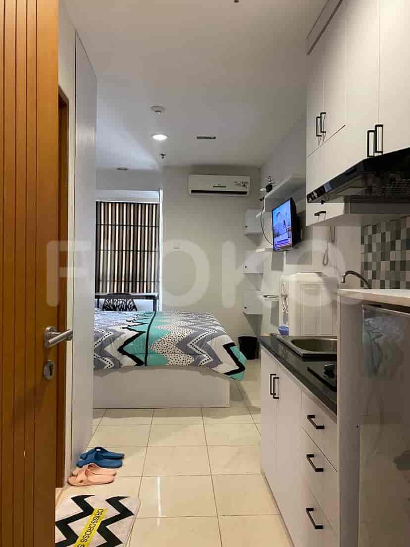 A view into a studio apartment showing the entrance, kitchen, and bedroom with a bed.