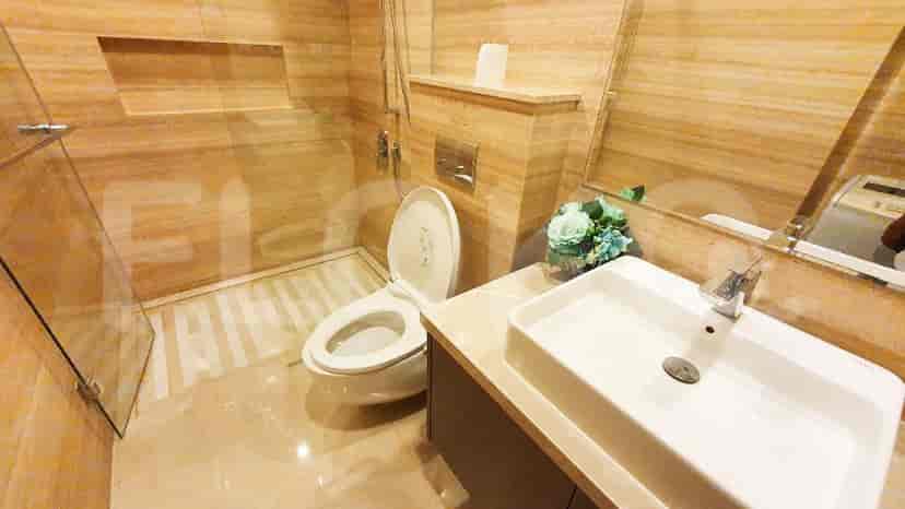 A modern bathroom with a marble finish, featuring a toilet, sink, and a glass-enclosed shower.