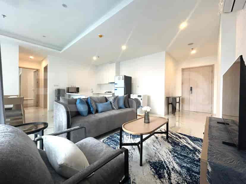 A modern living room with a grey sofa, coffee table, rug, and a view of the kitchen and dining area.