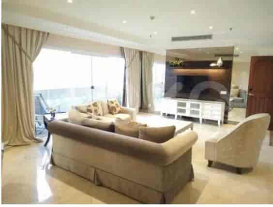 A spacious living room with an L-shaped grey sofa, wall-mounted smart TV, and large window with sheer curtains.