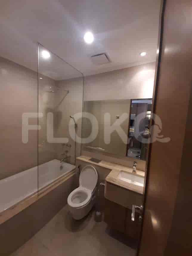 Kamar mandi modern dengan bak mandi, penutup pancuran kaca, dan toilet.