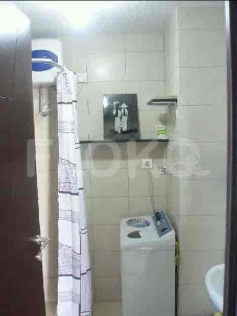 Kamar mandi kecil dengan area pancuran, mesin cuci, dan rak.