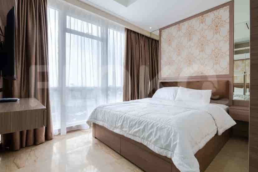 A bedroom with a large bed, windows with sheer curtains, and a small desk with a TV.