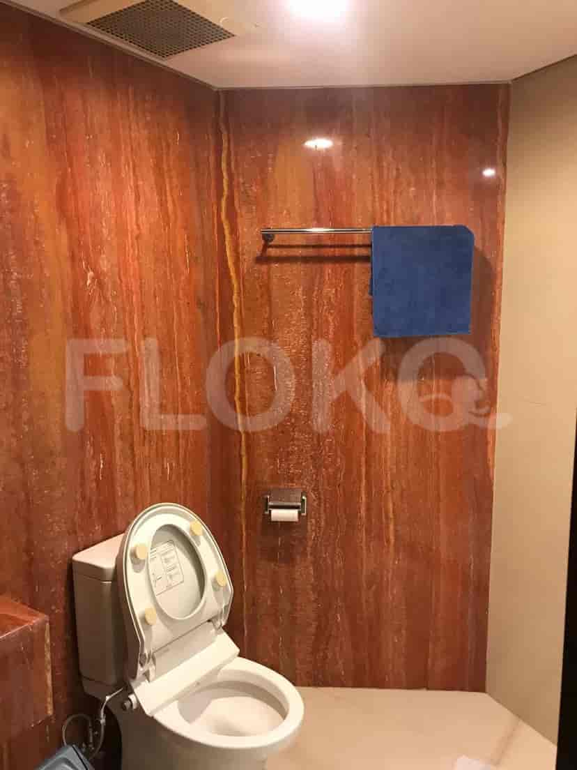 Kamar mandi dengan toilet, rak handuk, dan dinding batu.