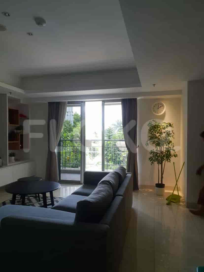 A living room featuring a grey sofa, a large window with curtains, and an outdoor view.