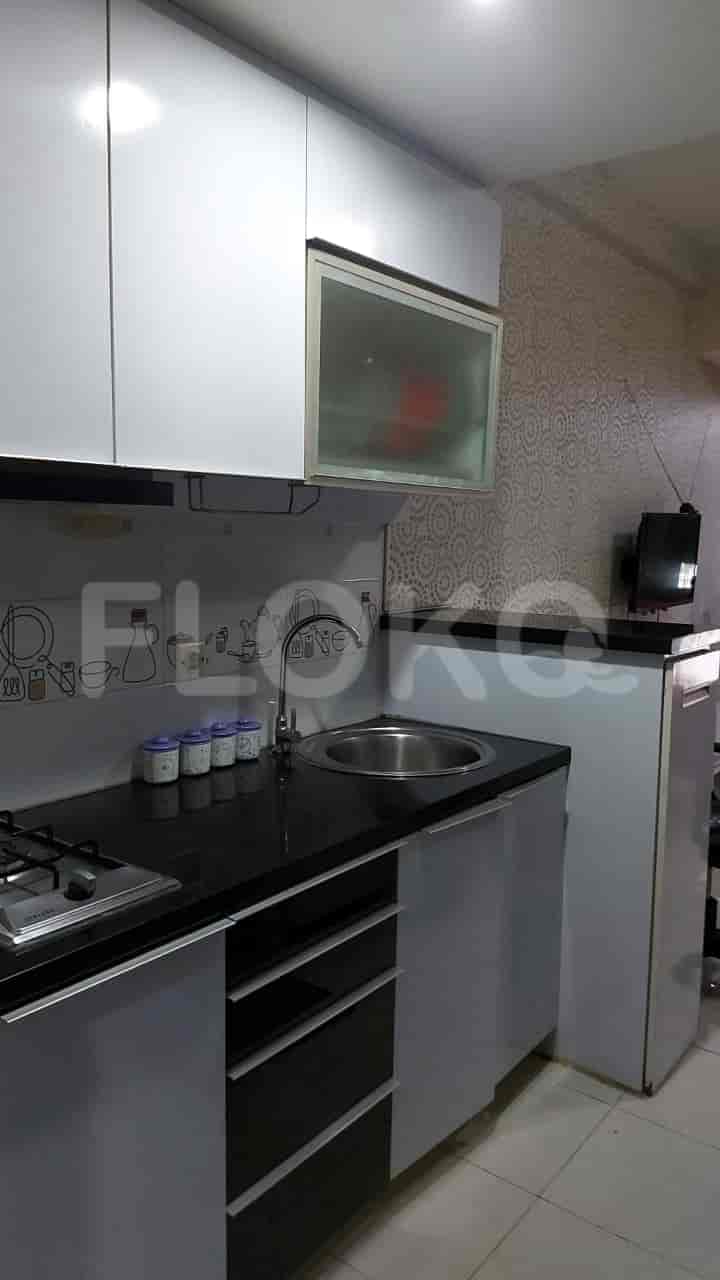 Dapur kecil dengan lemari putih, meja hitam, dan bak cuci piring baja tahan karat.