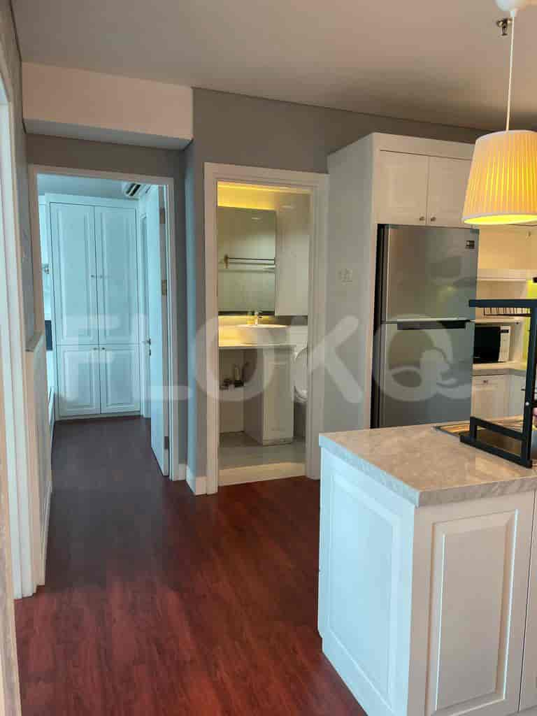 A hallway leads to a kitchen, showing white cabinetry, dark wooden flooring, and a modern design.