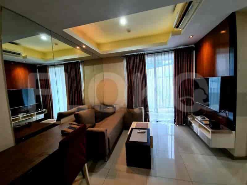 A spacious living room with an L-shaped grey sofa, wall-mounted smart TV, and large window with sheer curtains.