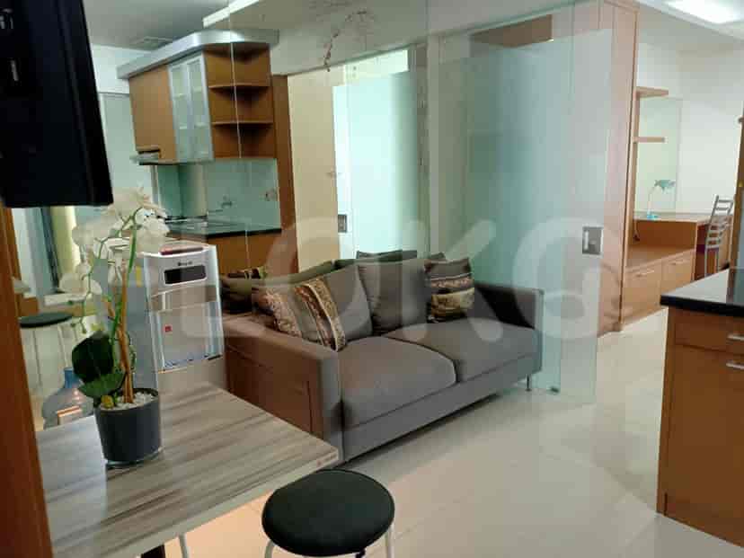 Ruang tamu modern dengan sofa abu-abu, area dapur, dan dispenser air.