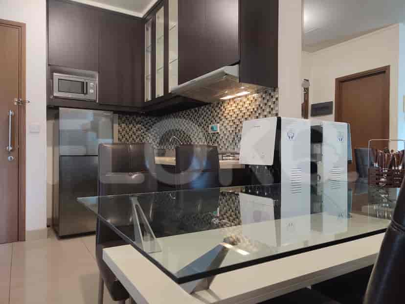 Area dapur dan ruang makan modern dengan lemari kayu gelap, meja kaca, dan dispenser air.