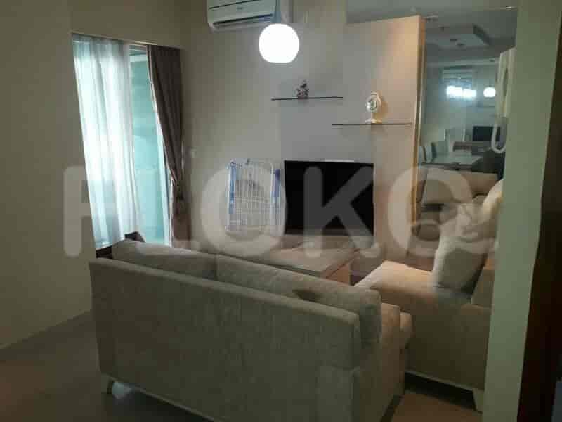 Ruang tamu dengan sofa berwarna terang, TV, dan jendela besar.