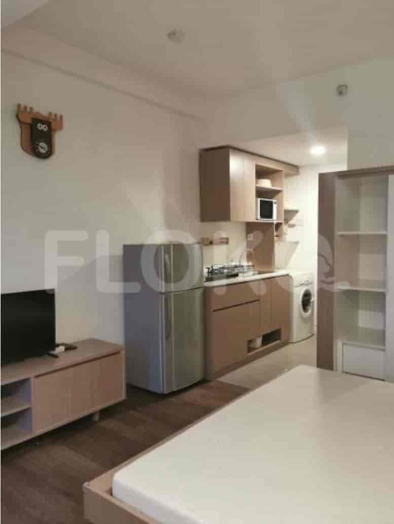 Compact studio with integrated kitchen, wooden furniture, and a bed, emphasizing space efficiency.
