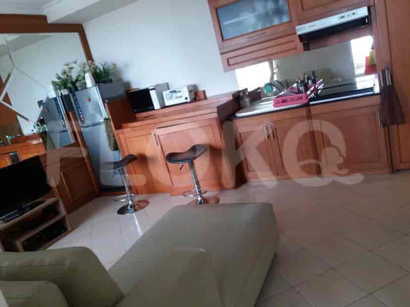 Kitchen area with wooden cabinets, bar stools, refrigerator, and a partial view of the living area with a sofa.