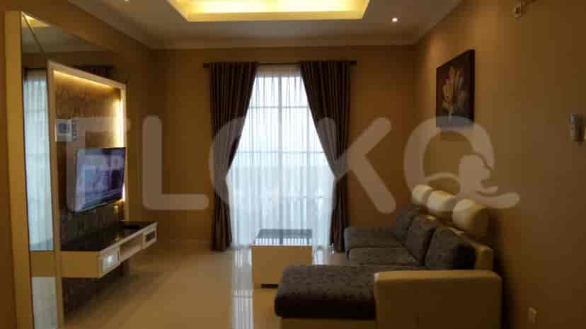 A spacious living room with an L-shaped grey sofa, wall-mounted smart TV, and large window with sheer curtains.