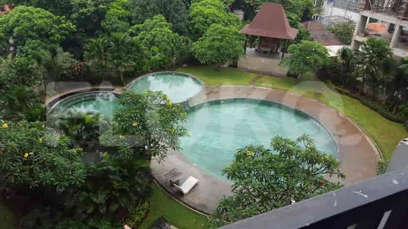A view of a swimming pool and surrounding green area from a balcony.