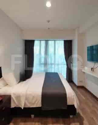 A well-lit bedroom with a double bed, curtains, and a TV mounted on the wall.