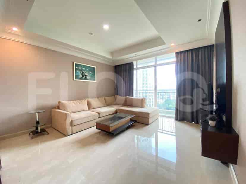 A spacious living room with an L-shaped beige sofa, a glass coffee table, and large windows.