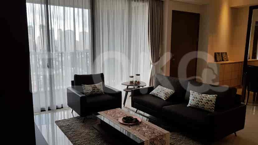 A modern living room featuring an L-shaped grey sofa, coffee table with decor, and large windows with sheer curtains.
