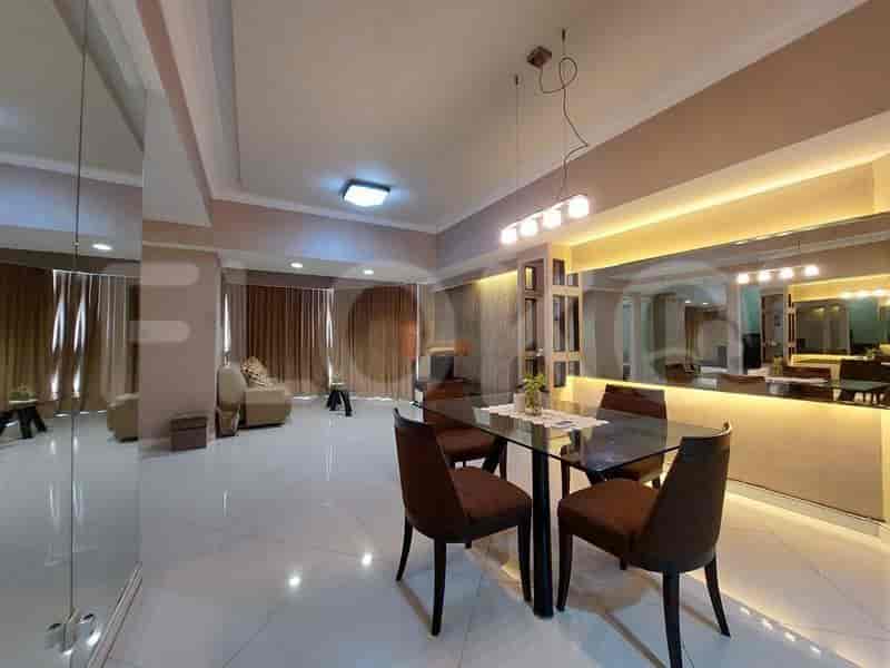 A well-lit dining area with a glass table and chairs, connected to a living area with a sofa and mirror.