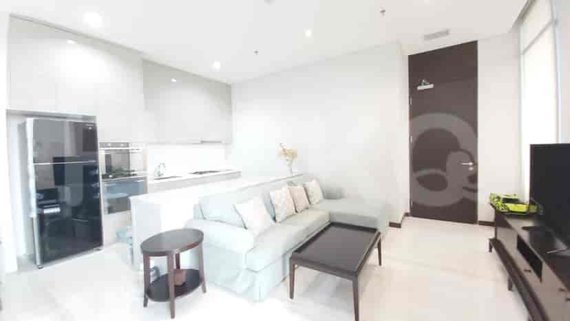 A modern apartment featuring a living room with an L-shaped sofa, connected to a kitchenette with a fridge and built-in oven.