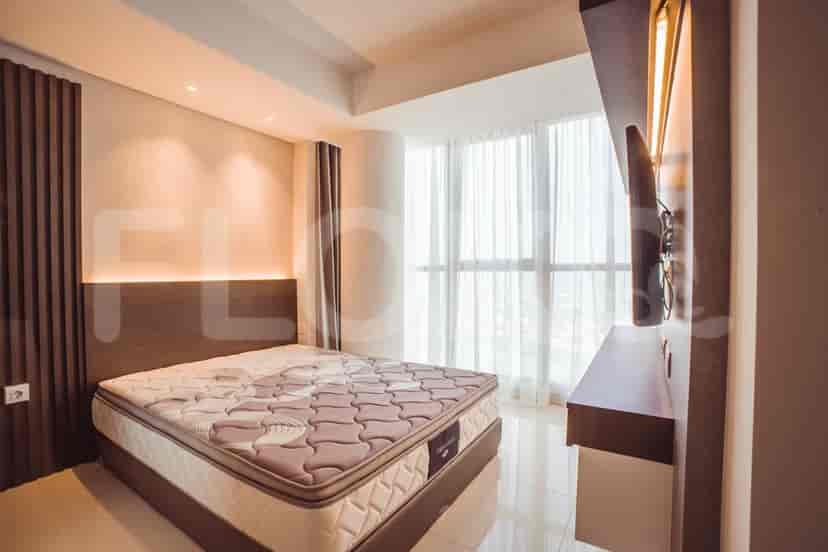 A modern bedroom with a large bed, a wall-mounted TV, and large windows with sheer curtains.