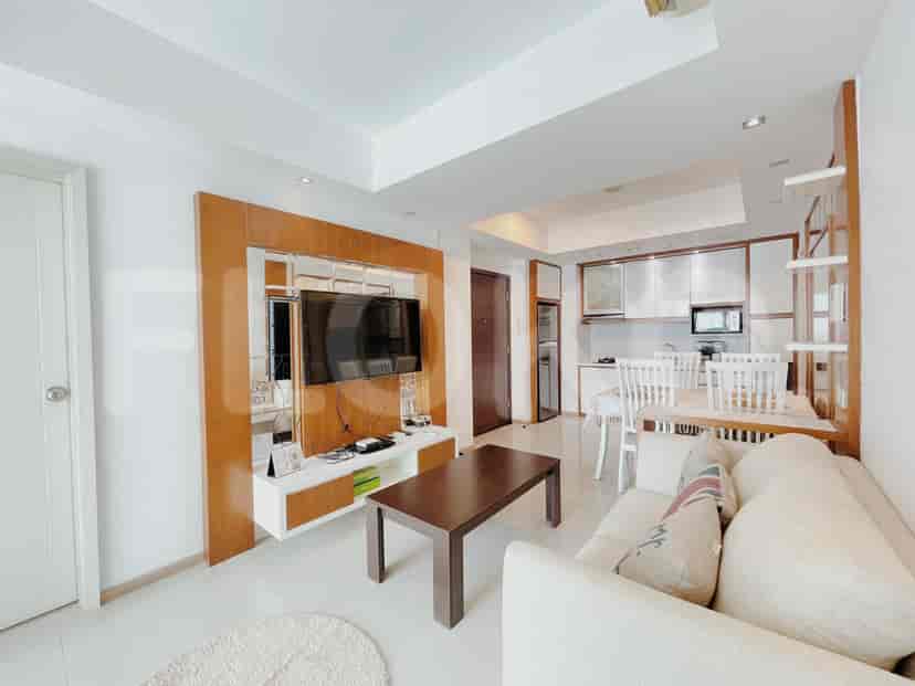 Ruang tamu yang cerah dengan sofa, TV, dan dapur terbuka.