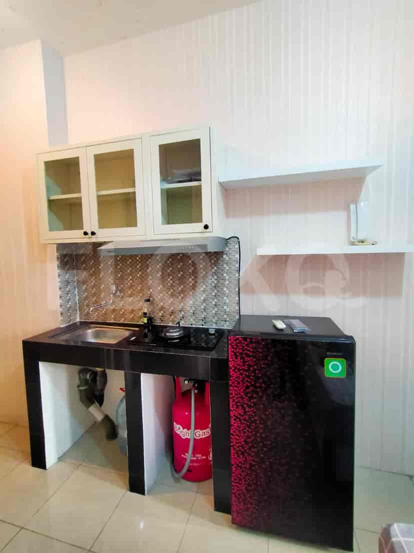 A compact kitchen with a gas stove, refrigerator, and overhead cabinets.