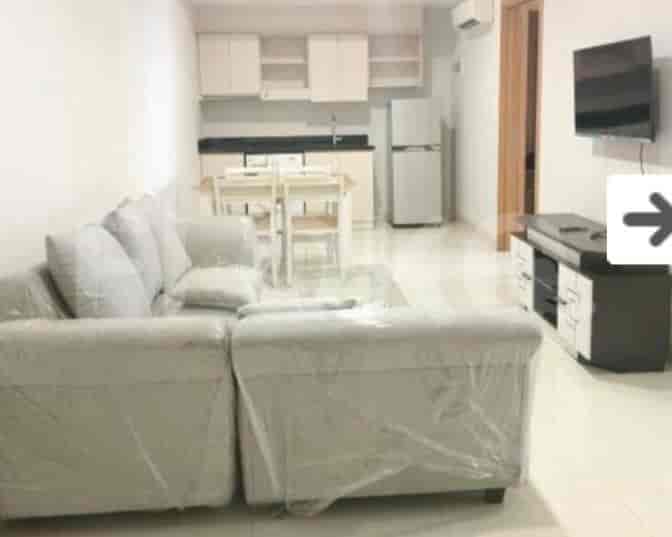 A living room with an L-shaped sofa, TV, and adjacent dining area.