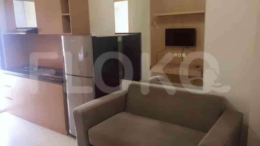 Dapur modern dengan lemari kayu, lemari es, dan area ruang tamu kompak dengan sofa dan TV.