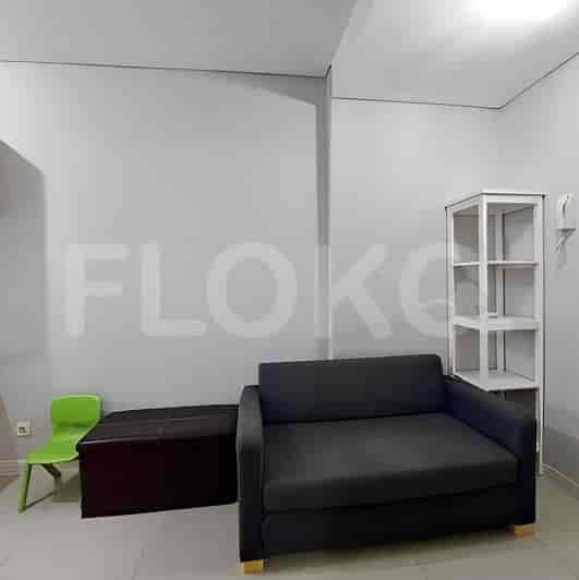 A studio apartment with a sofa, ottoman, and small green chair.
