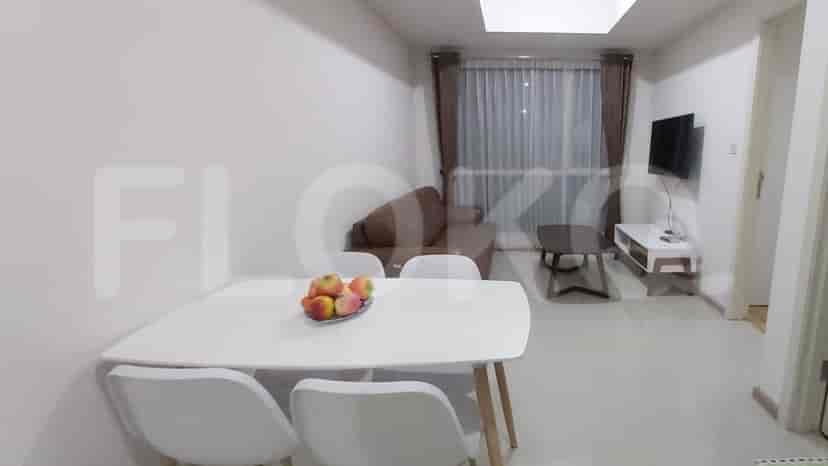 A living room with dining table and chairs. A window with sheer curtains is in the background.
