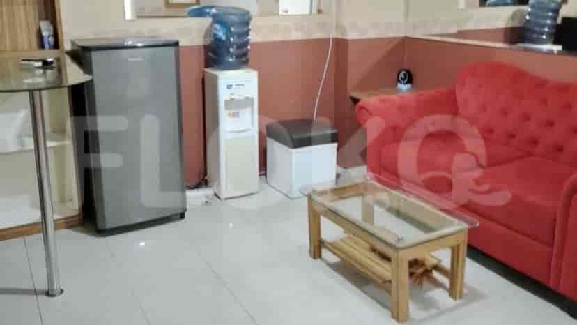Ruang tamu dengan sofa merah, meja kayu kecil, dan dispenser air.