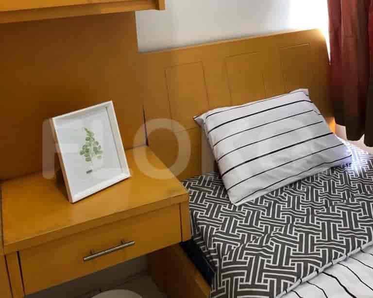 A bedroom featuring a bed with two cylindrical pillows and a wooden headboard and dresser.
