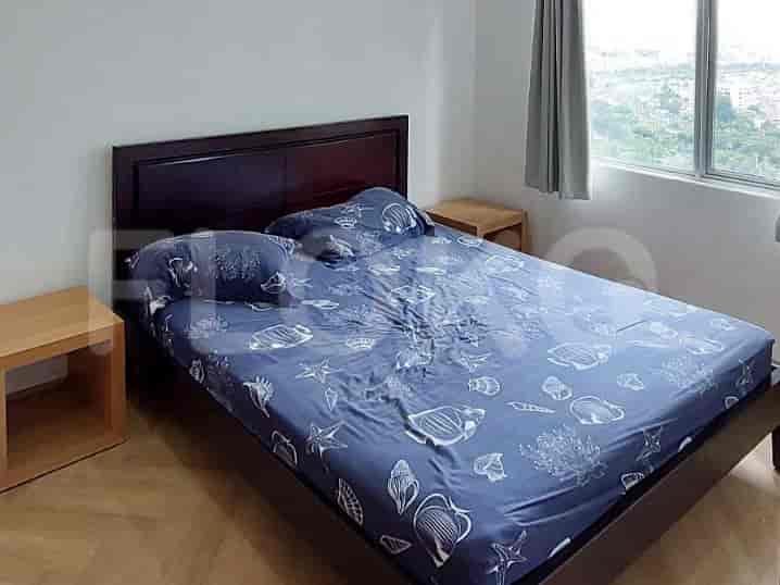 A bedroom featuring a bed with patterned bedding, two bedside tables, and a view of the city.