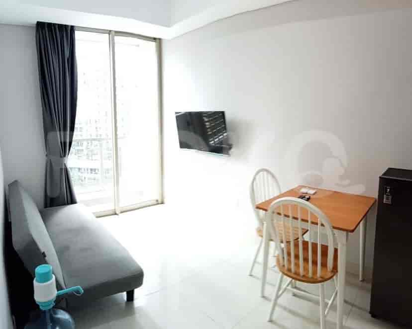 A combined living and dining area featuring a grey sofa, mounted TV, small dining set and large windows.