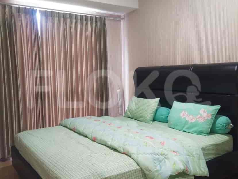 A bedroom featuring a large bed with a green comforter, pillows, and curtains.